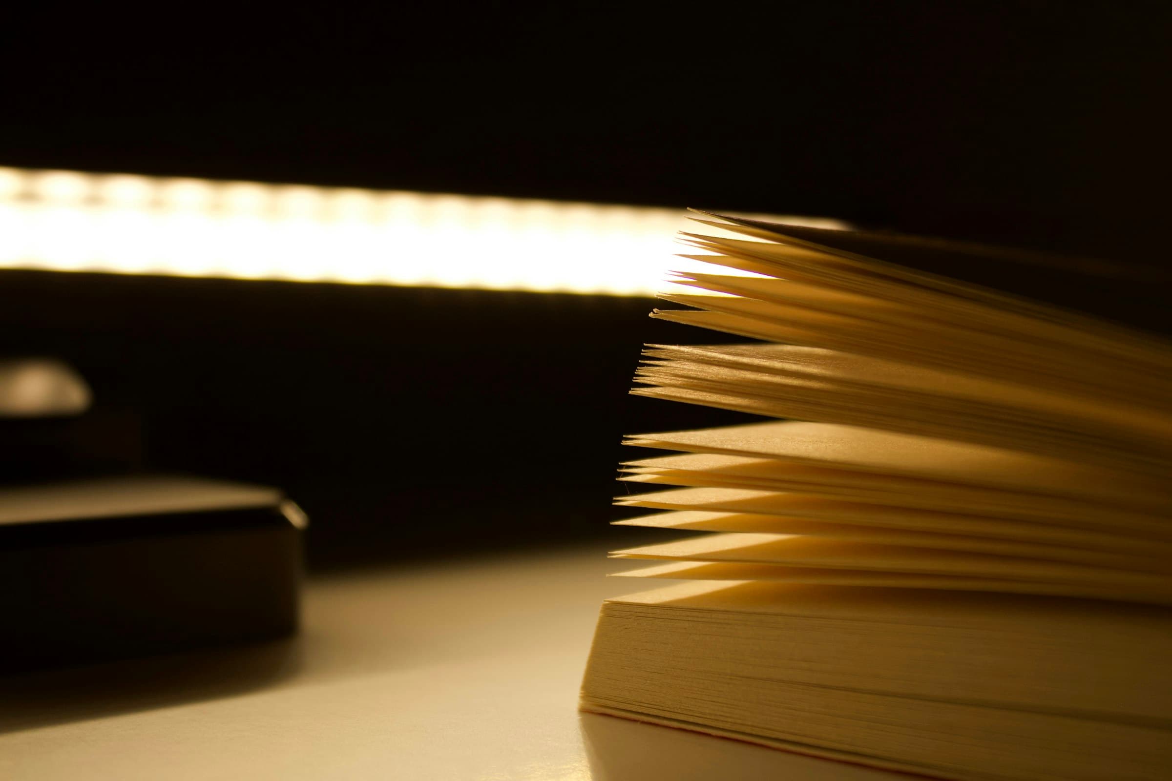 Hojas de un libro abierto iluminadas por una lámpara en un escritorio en penumbra